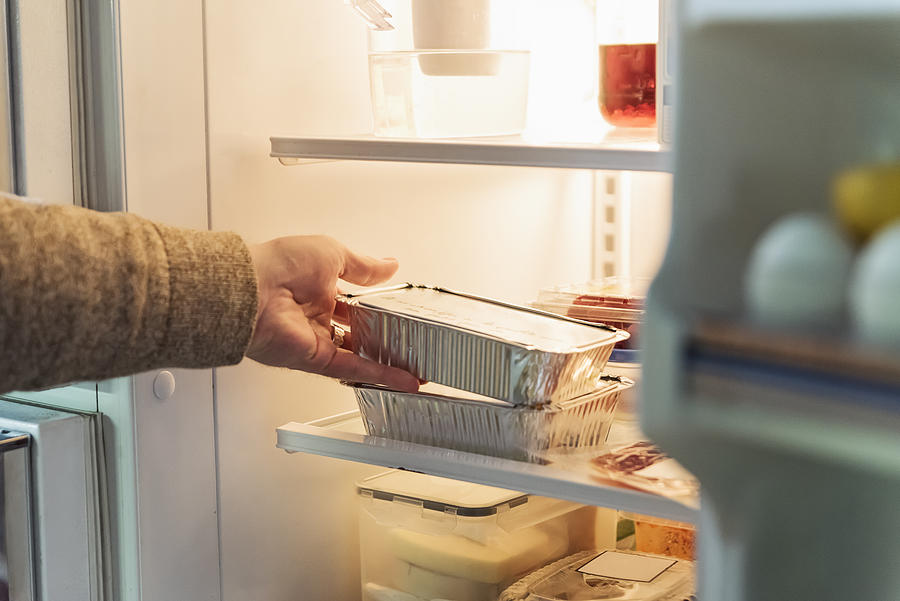 Mans hand taking takeout meal out of refrigerator. Photograph by Martinedoucet
