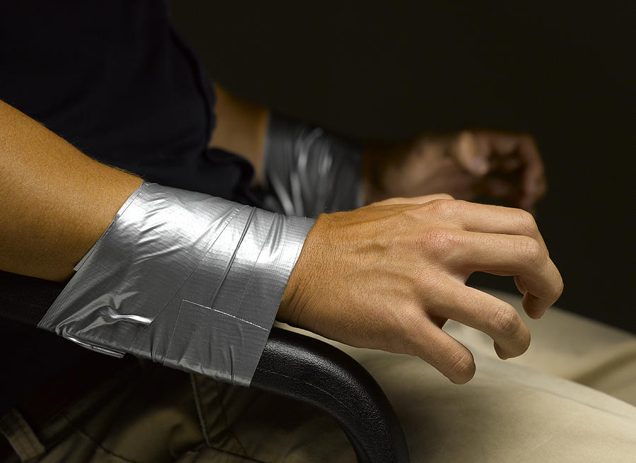 Mans wrists taped to arms of chair, close-up Photograph by Jeffrey Coolidge