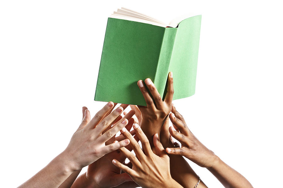 Many mixed hands reach for green-covered book against white Photograph by RapidEye