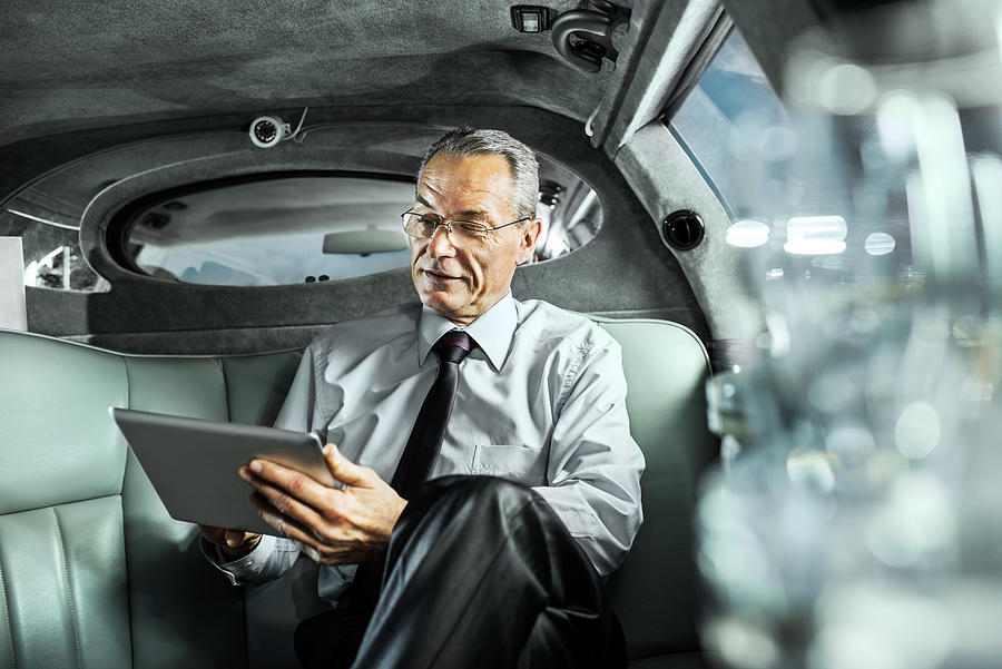 Mature adult businessman working on digital tablet in limousine. Photograph by Skynesher