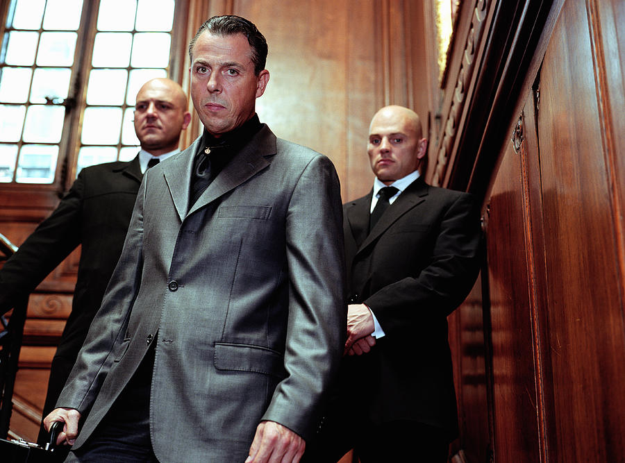 Mature businessman flanked by two security guards in panelled room, portrait Photograph by Digital Vision