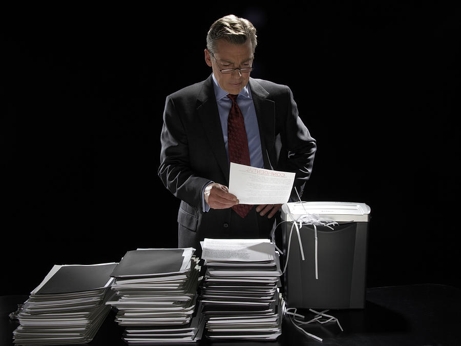 Mature businessman standing by shredder reading confidential document Photograph by James Woodson
