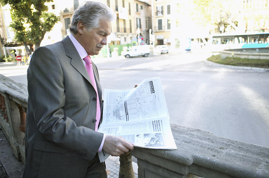 Mature Businessman Stands by a Road Reading a Newspaper Photograph by Digital Vision.