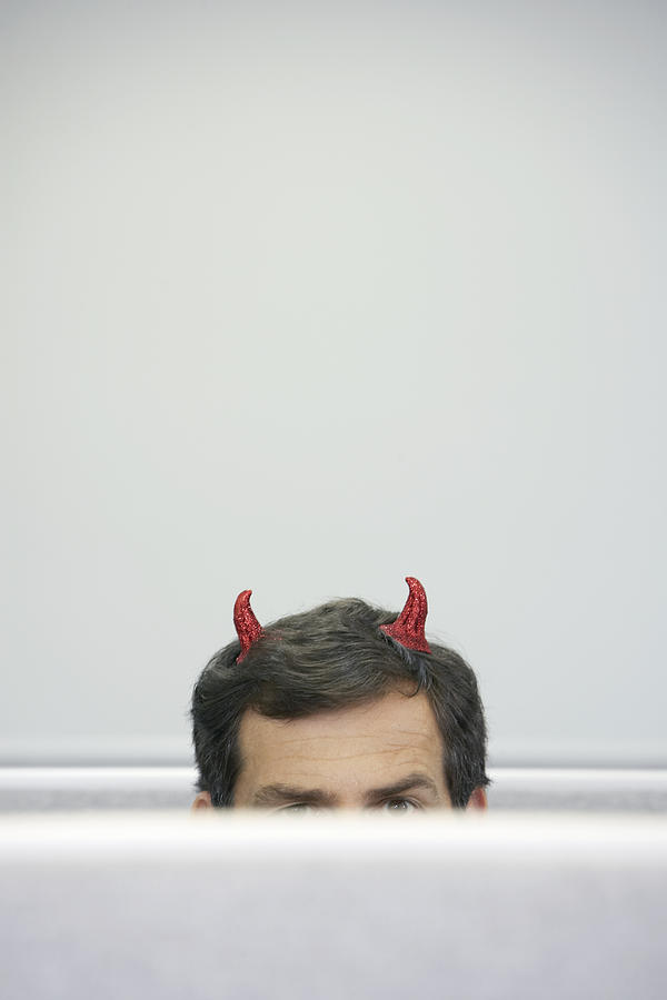 Mature businessman with devil horns sitting in cubicle, high section Photograph by Noel Hendrickson