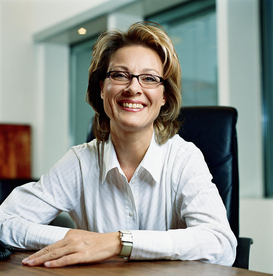 Mature businesswoman sitting at desk, smiling, portrait Photograph by Johannes Mann
