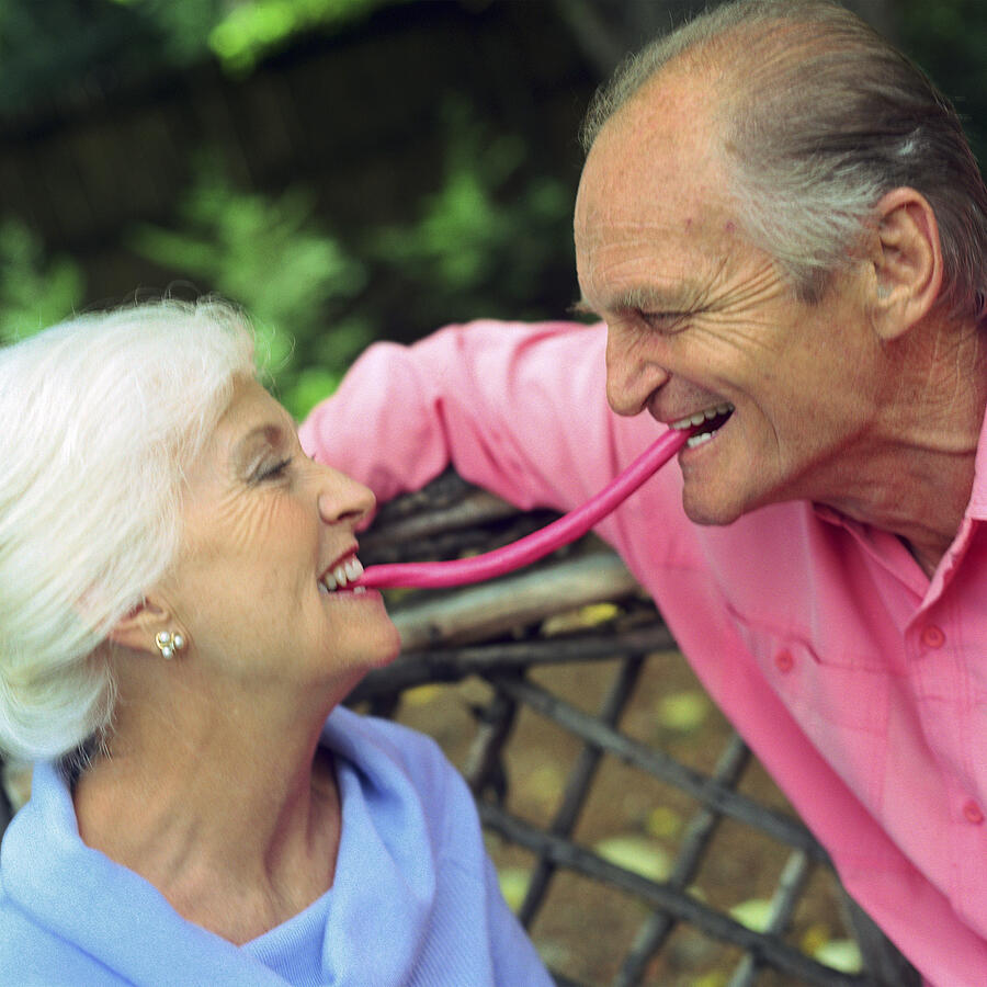 Mature couple face to face, each with one end of piece of candy in mouth between them Photograph by Patrick Sheandell OCarroll