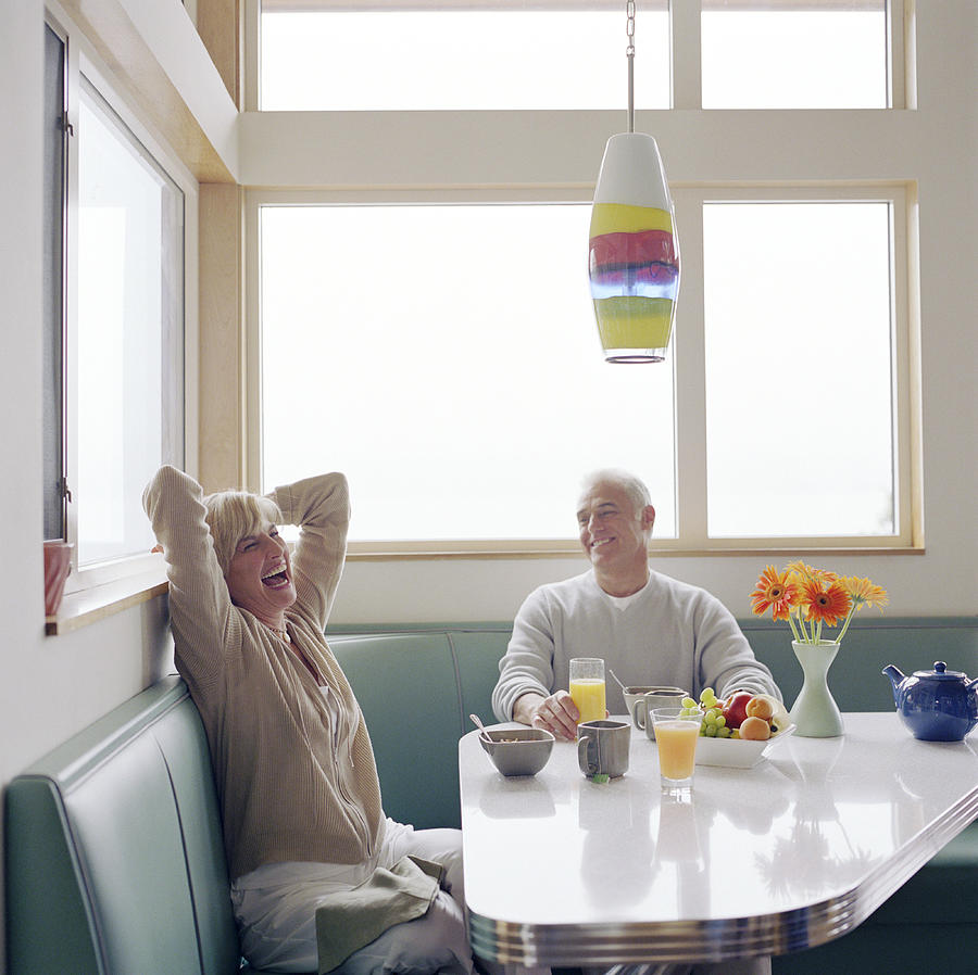 Mature couple laughing over breakfast Photograph by Ryan McVay
