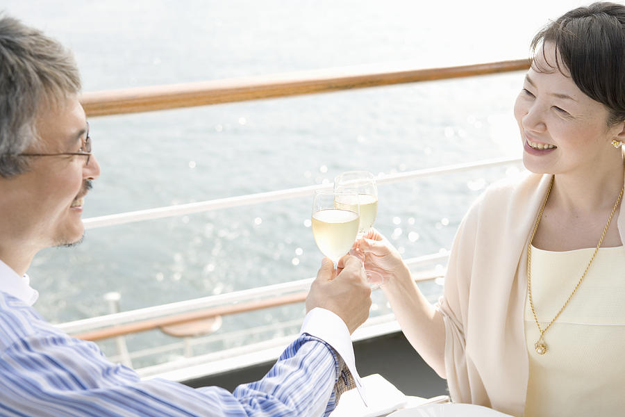 Mature couple toasting on deck of cruise ship, smiling Photograph by Indeed