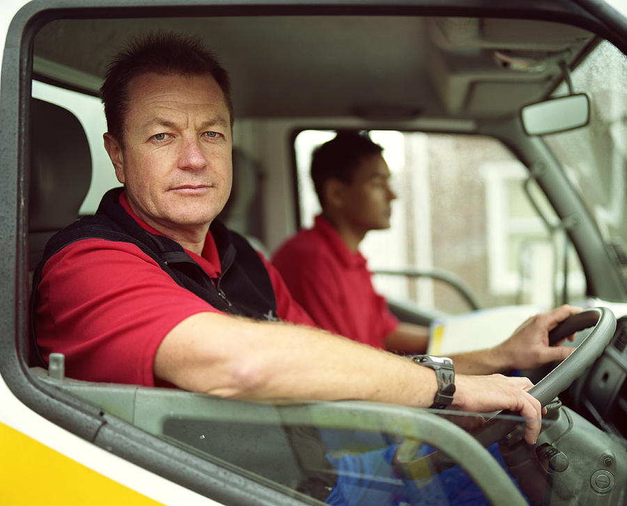 Mature delivery man at wheel of truck with colleague, portrait Photograph by Alistair Berg
