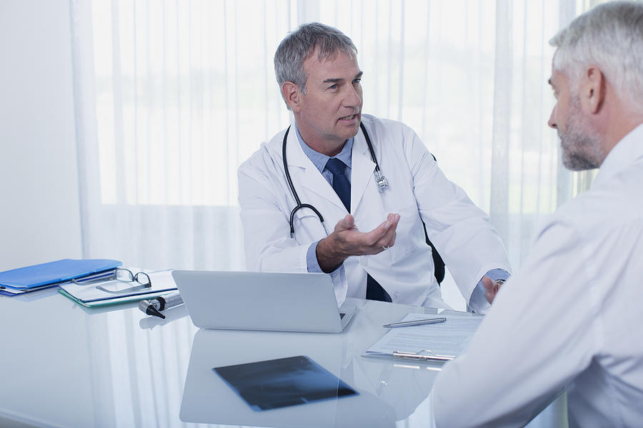 Mature doctor talking to patient at desk in office Photograph by Dan Dalton