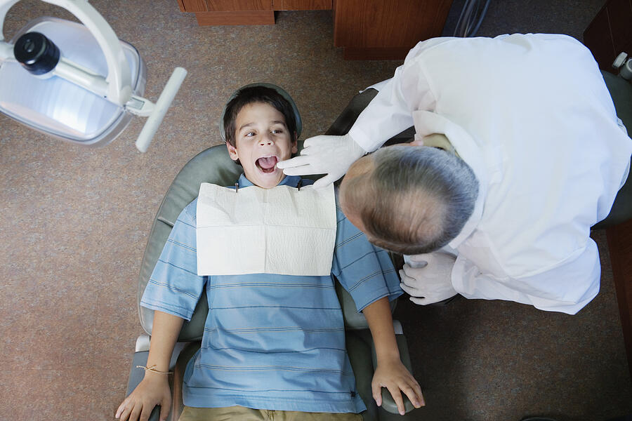 Mature male dentist examining boys (10-12) teeth, overhead view Photograph by Andersen Ross