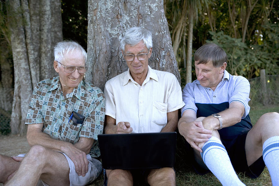 Mature man and senior men by tree, looking at laptop screen, smiling Photograph by Manchan