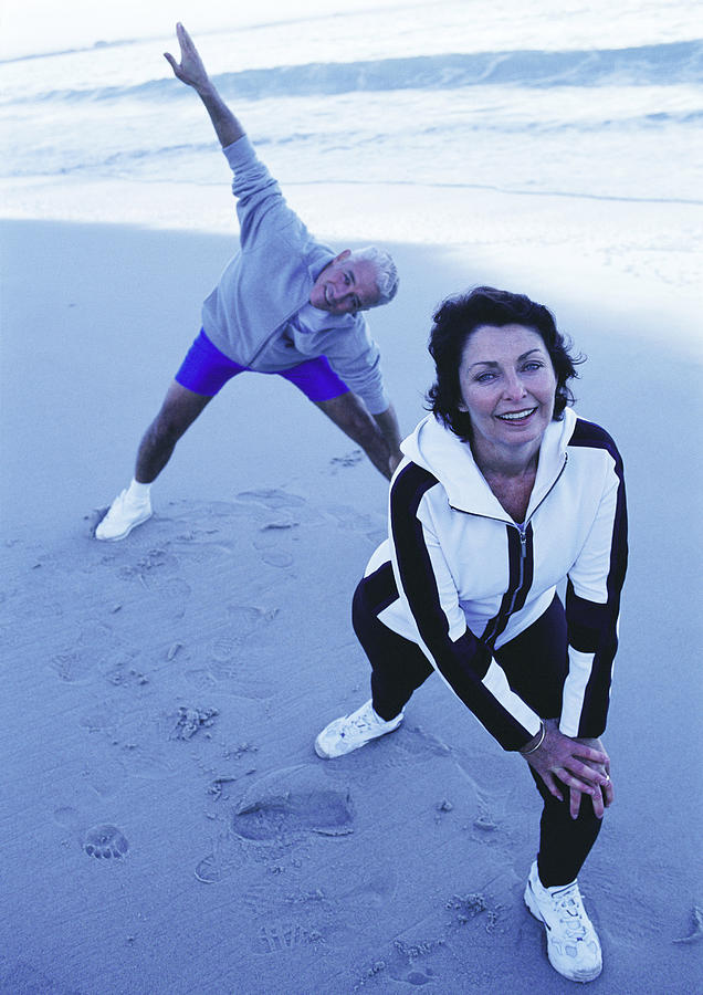 Mature man and woman warming up on beach Photograph by Vincent Hazat