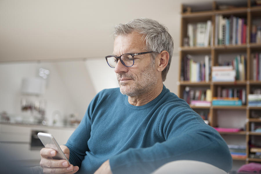 Mature man at home looking at cell phone Photograph by Westend61