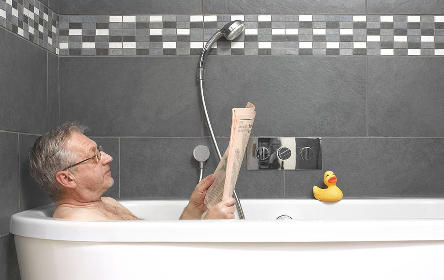 Mature man reading financial paper in bath Photograph by Peter Dazeley