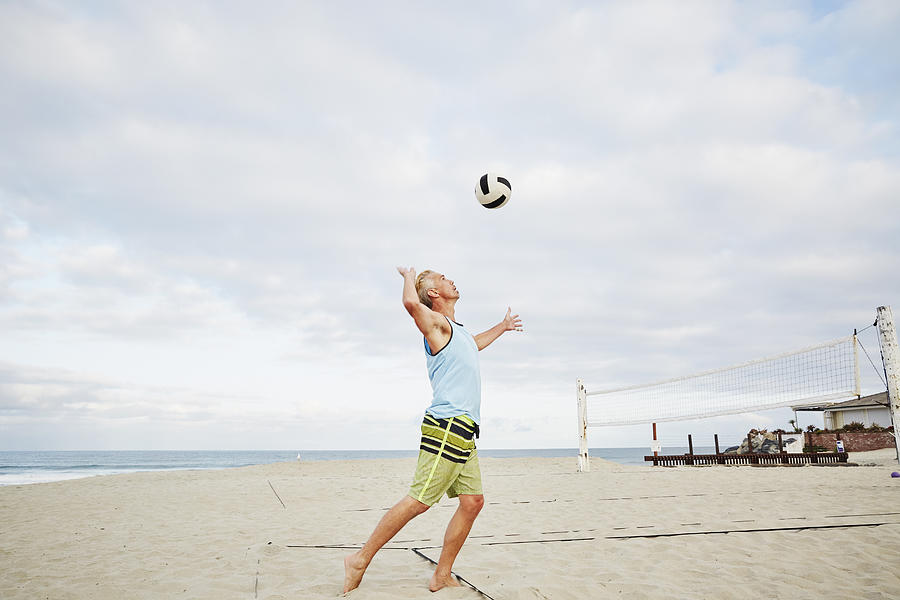 Mature man standing on a beach, playing beach volleyball.  Photograph by Mint Images