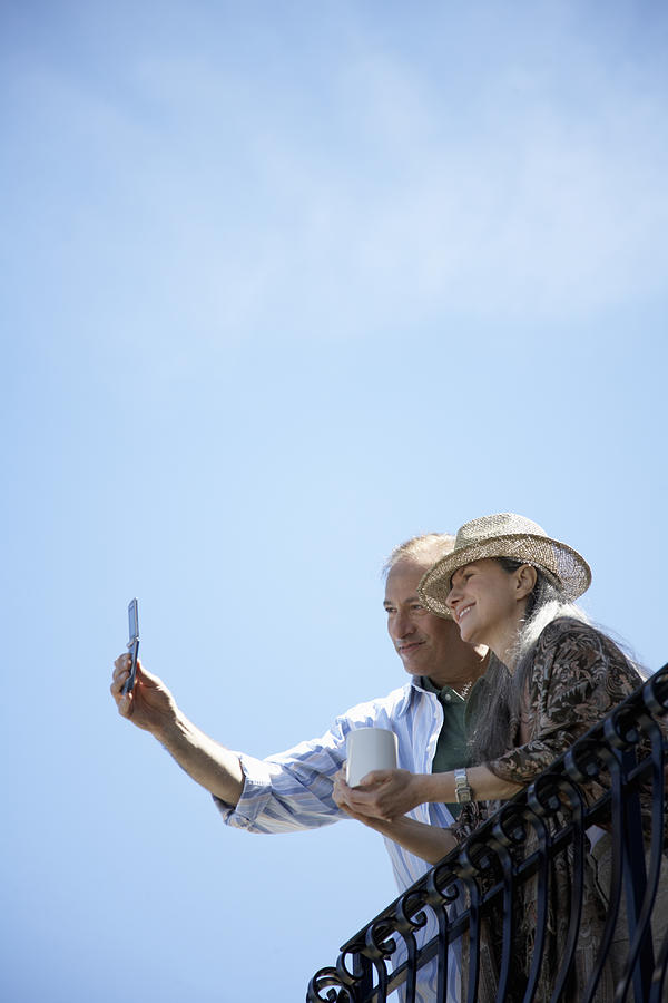 Mature man taking picture on balcony with camera phone, low angle view Photograph by Sean Justice
