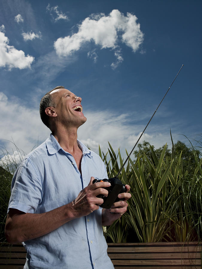 Mature man using radio controlled handset outdoors, looking up and laughing Photograph by Dave Nagel