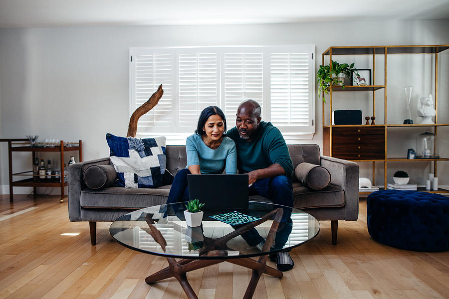 Mature married couple at home on the sofa looking at laptop Photograph by Counter
