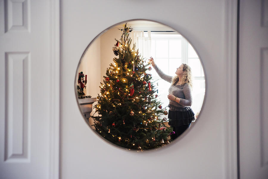 Mature woman decorating Christmas tree at home. Photograph by Martinedoucet
