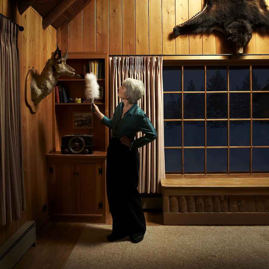 Mature woman dusting with feather duster Photograph by Thomas Northcut