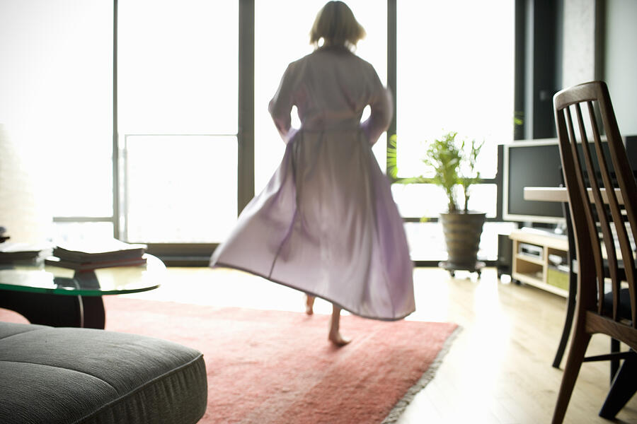 Mature woman in bathrobe walking across living room, rear view Photograph by Charles Gullung