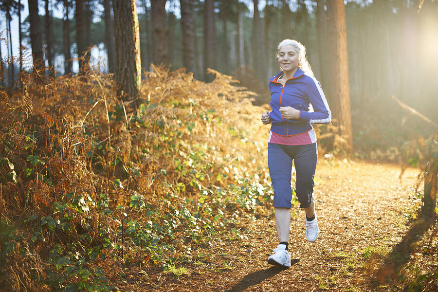 Mature woman jogging on forest path Photograph by Peter Muller