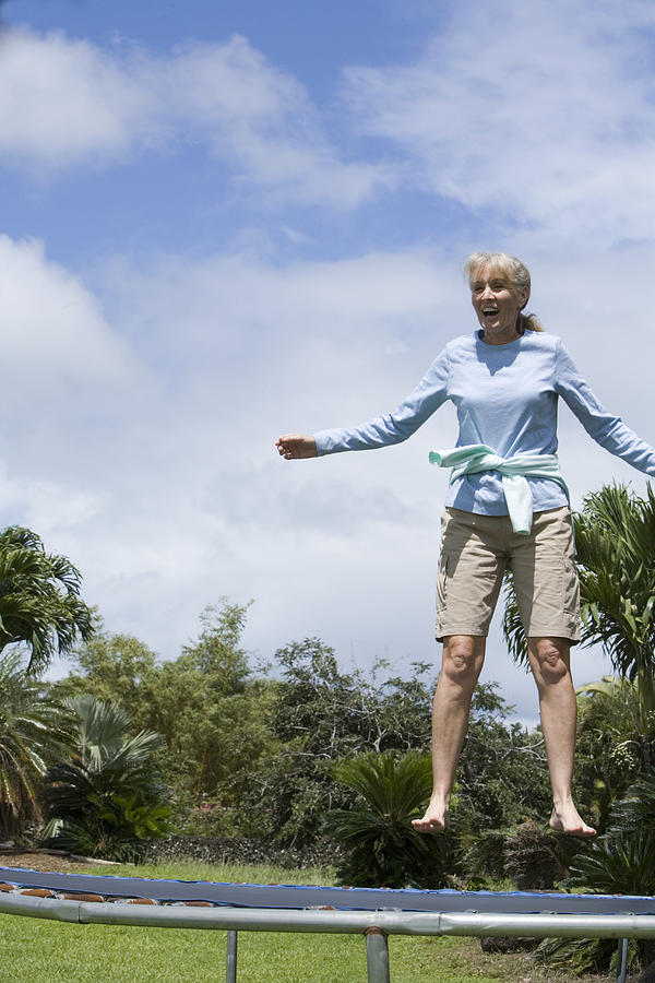 Mature woman jumping on trampoline, low angle view Photograph by Caroline Woodham