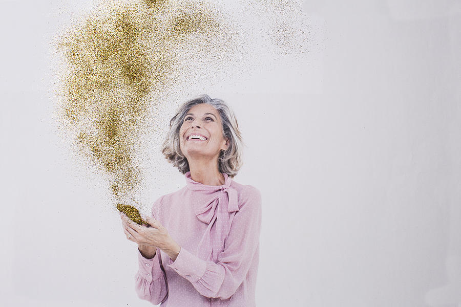 Mature woman looking at gold dust from phone Photograph by Emma Innocenti