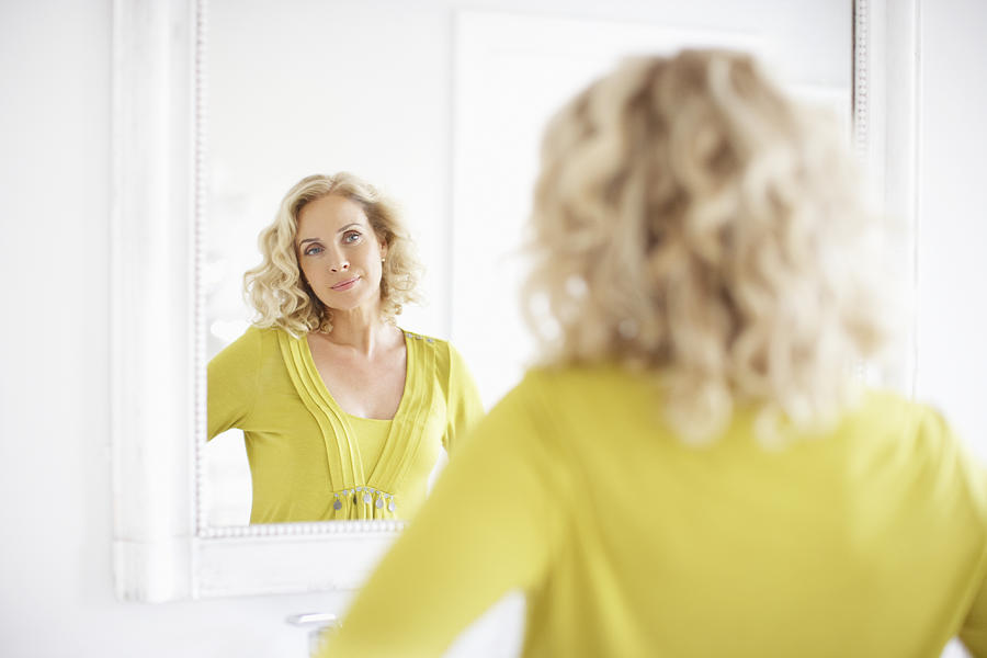 Mature woman looking in mirror Photograph by Newton Daly
