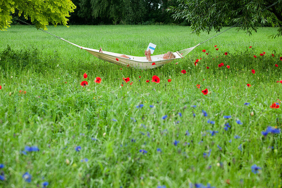 Mature woman lying on hammock in garden reading book Photograph by RelaxFoto.de