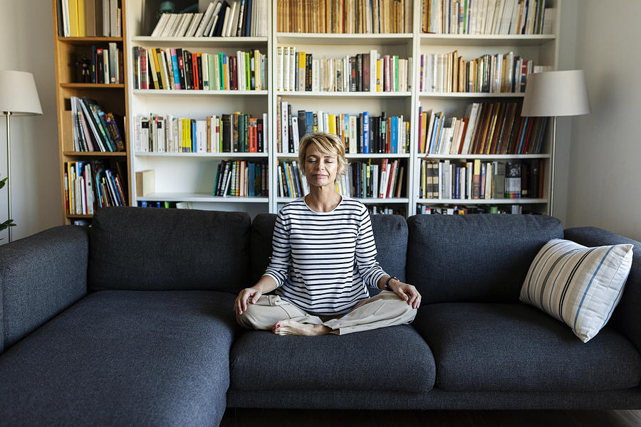 Mature woman practicing yoga on couch at home Photograph by Westend61