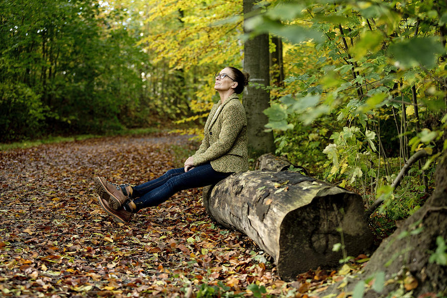 Mature woman sitting on a tree trunk in a autumn forest Photograph by Westend61