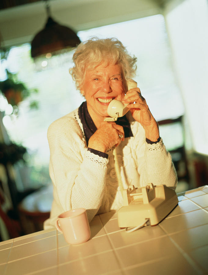 Mature woman talking on phone in kitchen Photograph by Antony Nagelmann