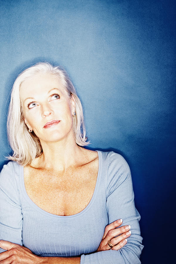 Mature woman thinking against blue background Photograph by GlobalStock