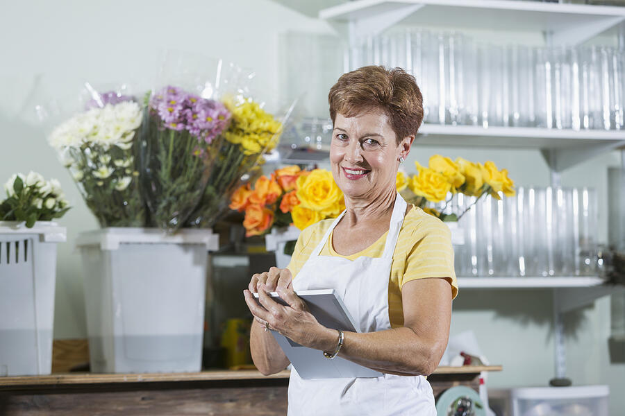 Mature woman working in flower shop using digital tablet Photograph by Kali9