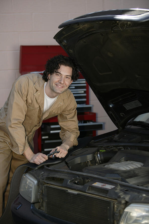 Mechanic posing with car in shop Photograph by Comstock
