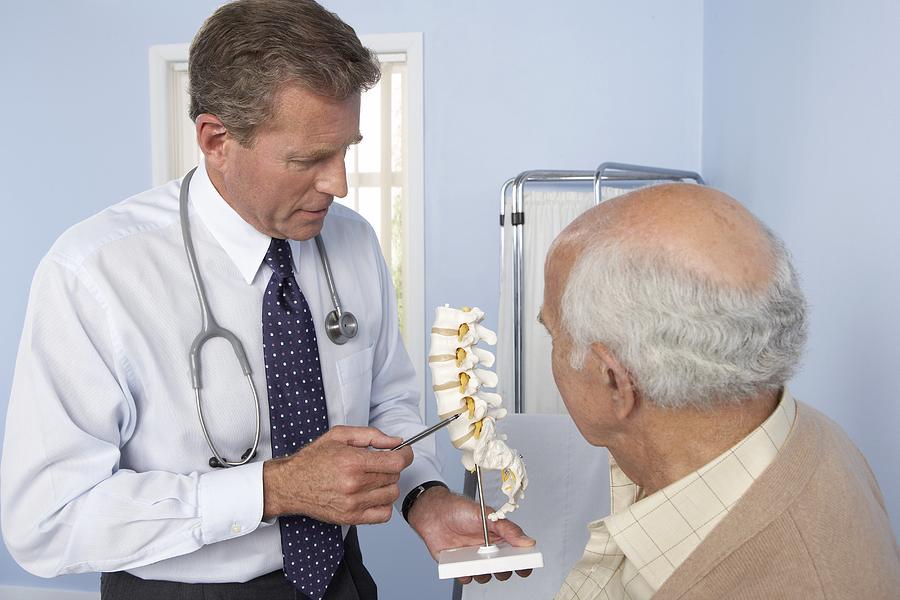 Medical consultation, general practitioner refers to model of spine while discussing elderly patient Photograph by Adam Gault/spl