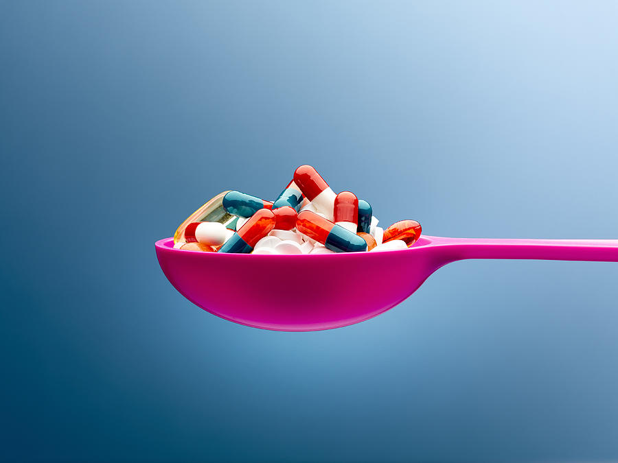 Medicine capsules in pink spoon against blue background Photograph by Caia Image