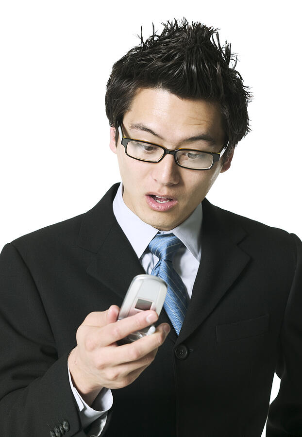 Medium Shot Of A Young Adult Business Man As He Acts Surprised At Something On His Cell Phone Photograph by Photodisc