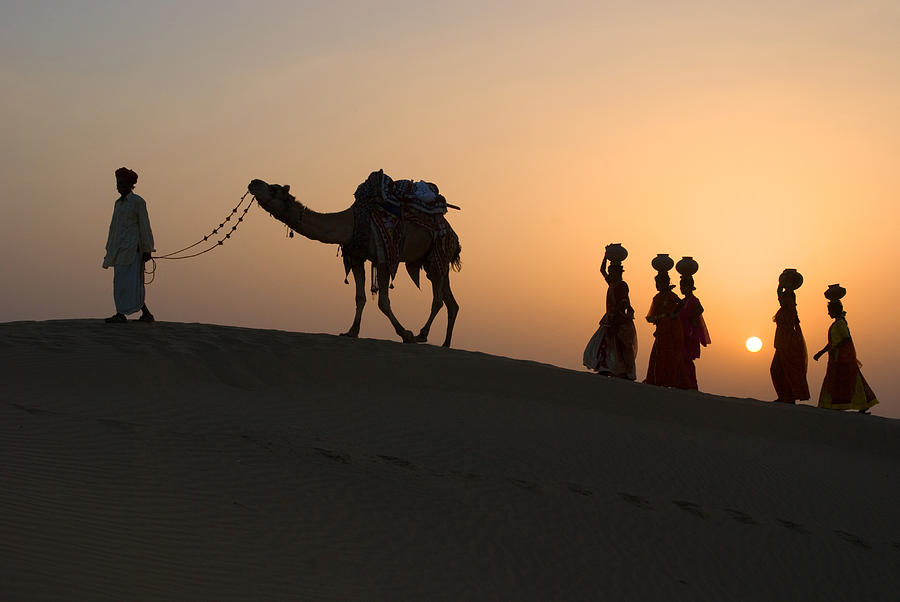 Men and woman with camel climbing up sand dune of khuhri, Jaisalmer, Rajasthan, India Photograph by Dinodia Photo