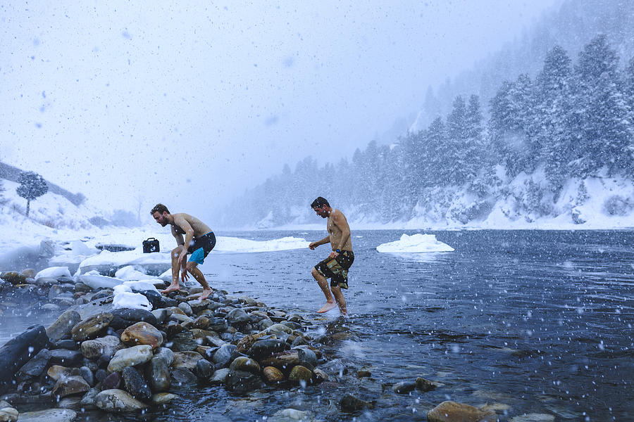 Men walking on stones in river during snowfall Photograph by Cavan Images