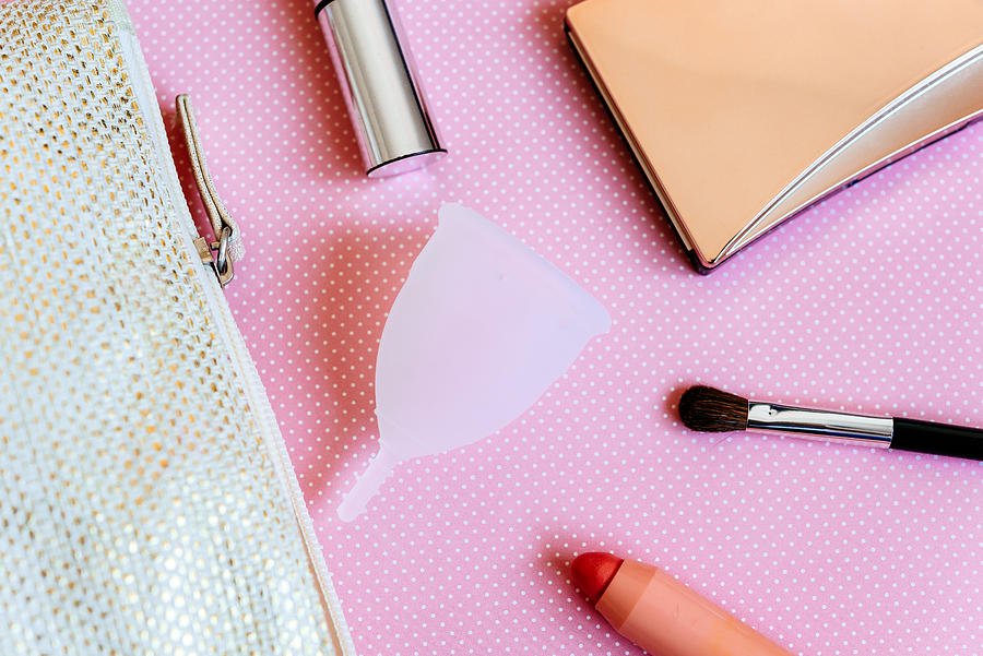 Menstrual cup and make-up on pink background Photograph by Volanthevist
