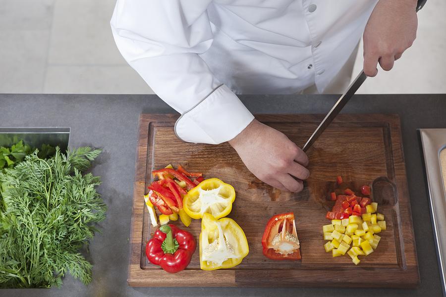 Mid- adult chef dices red and yellow bell peppers Photograph by Moodboard