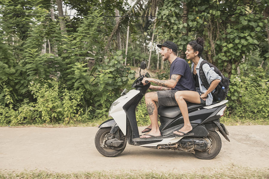 Mid adult couple riding moped through forest, side view Photograph by JohnnyGreig