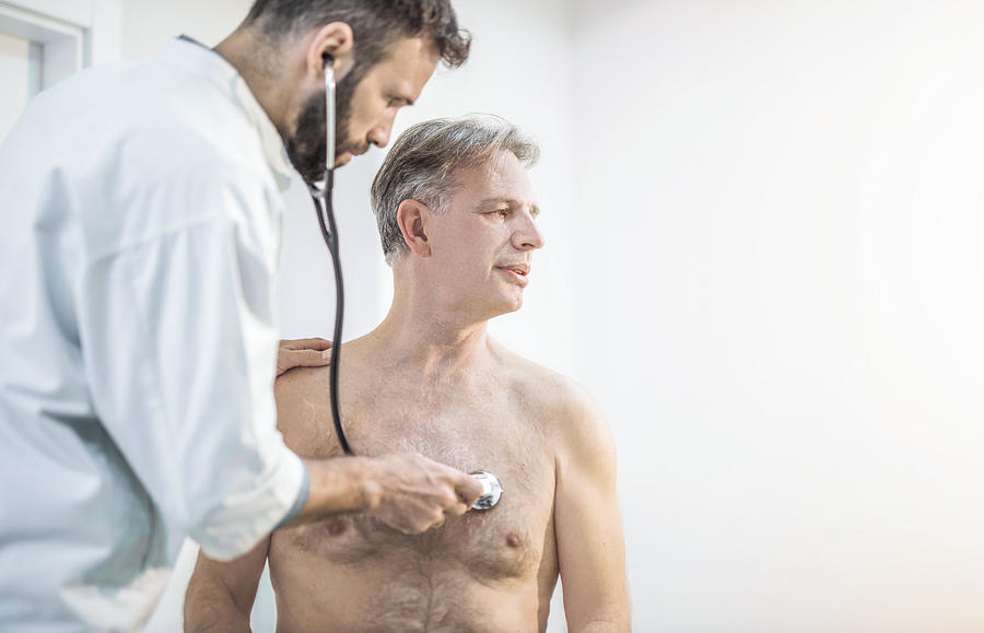 Mid adult doctor examining his senior patients chest. Photograph by DjelicS
