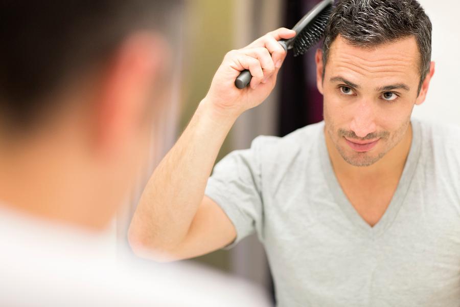 Mid adult man, looking in mirror, brushing hair Photograph by Steven C. De La Cruz