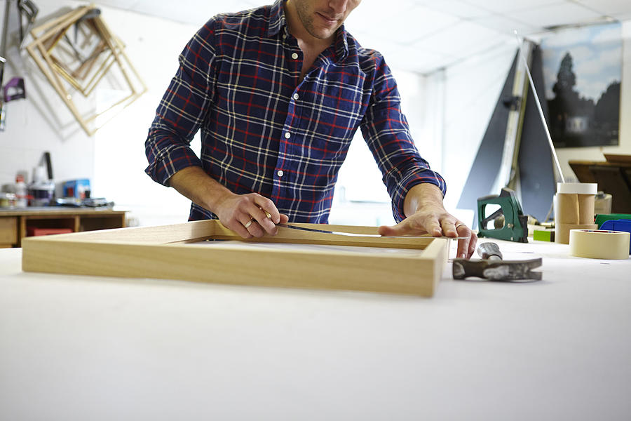 Mid adult man measuring frame on workbench in picture framers workshop Photograph by Janie Airey