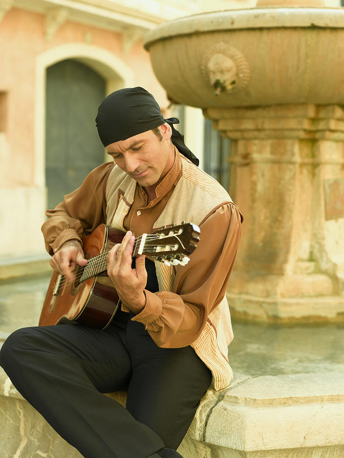 Mid adult man playing a guitar and looking down Photograph by Denkou Images