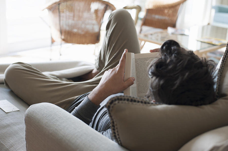 Mid adult man relaxing on sofa, reading book, rear view Photograph by Bettina Mare Images